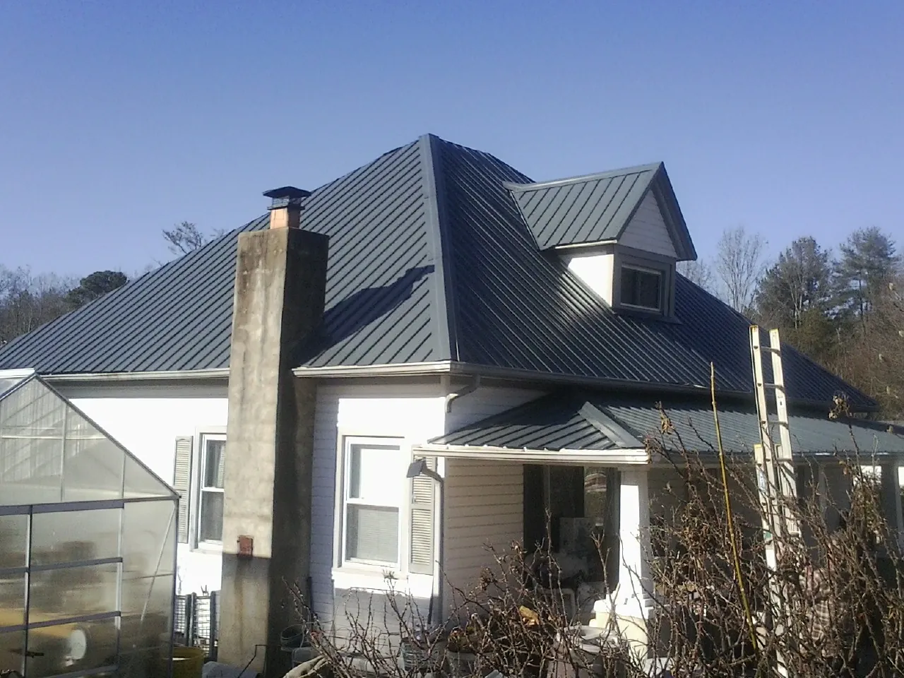 Dark blue standing seam metal roof on a white farmhouse with dormer — Slate & Tile Roof Repair by Roofing Brothers in Washburn