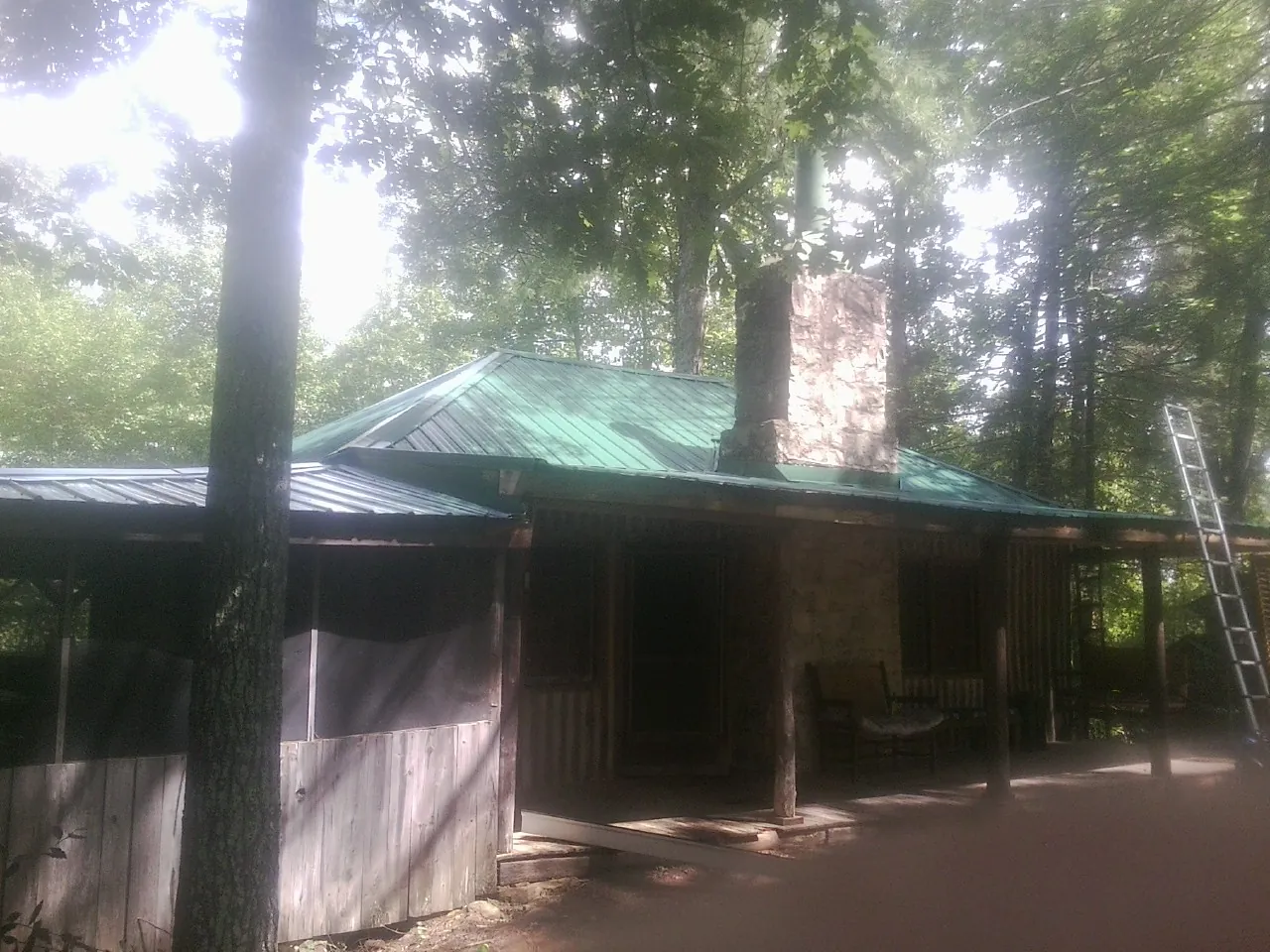Green metal roof and stone chimney above a log cabin porch in Washburn