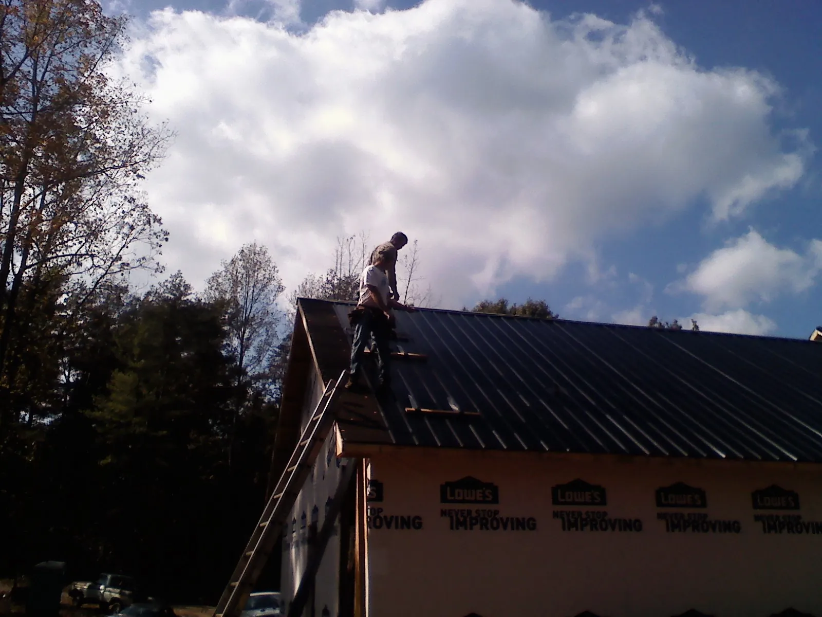Roofer fastening dark metal panels high against a cloudy sky, from a Roof Inspection job in Washburn