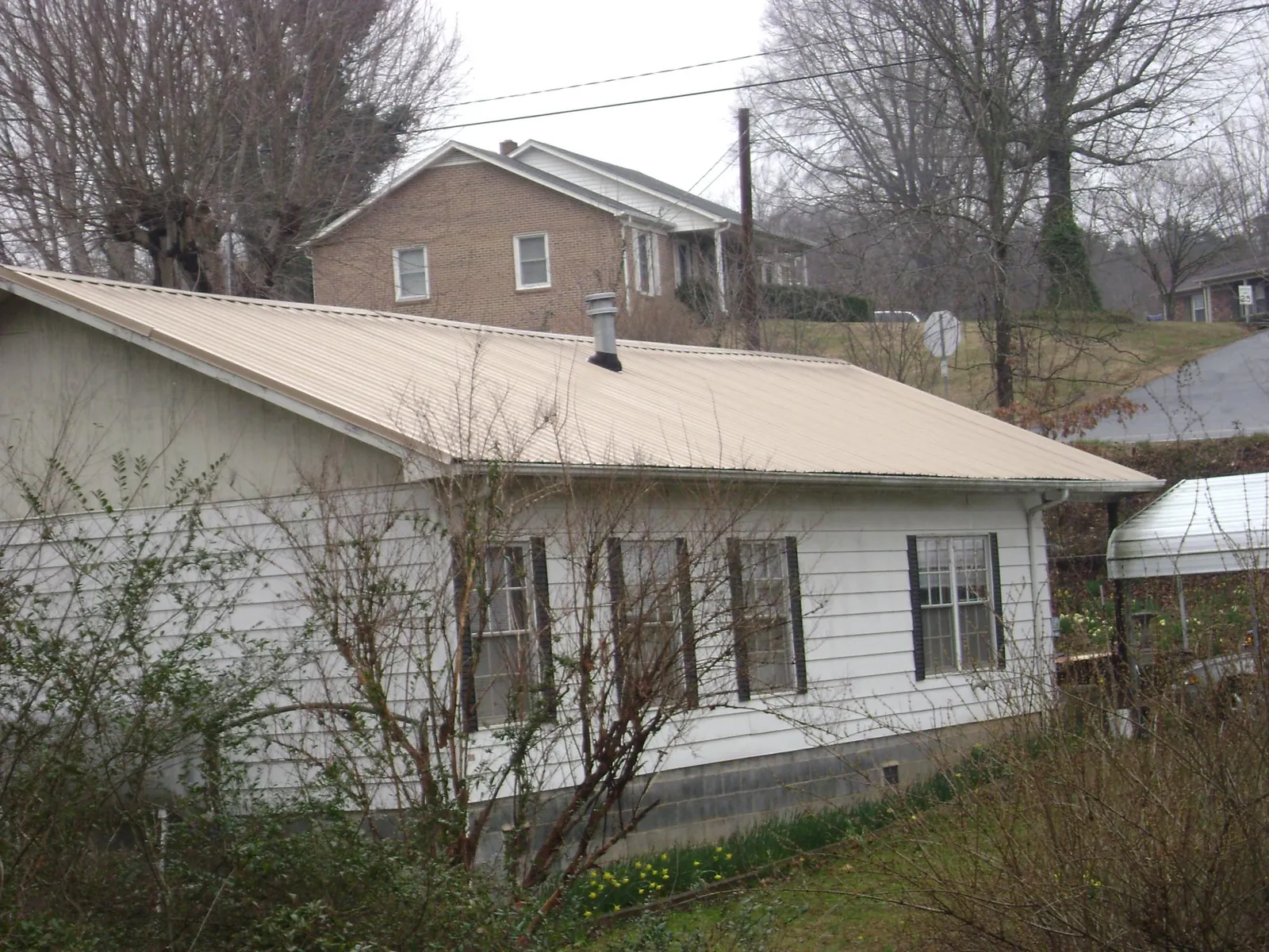 Tan metal roof on a white sided house set into a hillside — Commercial Roofing by Roofing Brothers in Washburn